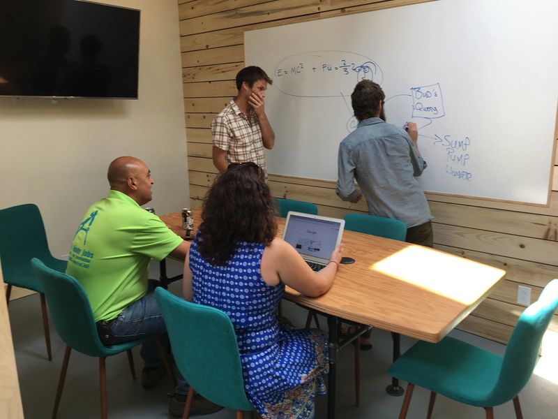 Five people in a meeting room collaborating on a whiteboard with equations.