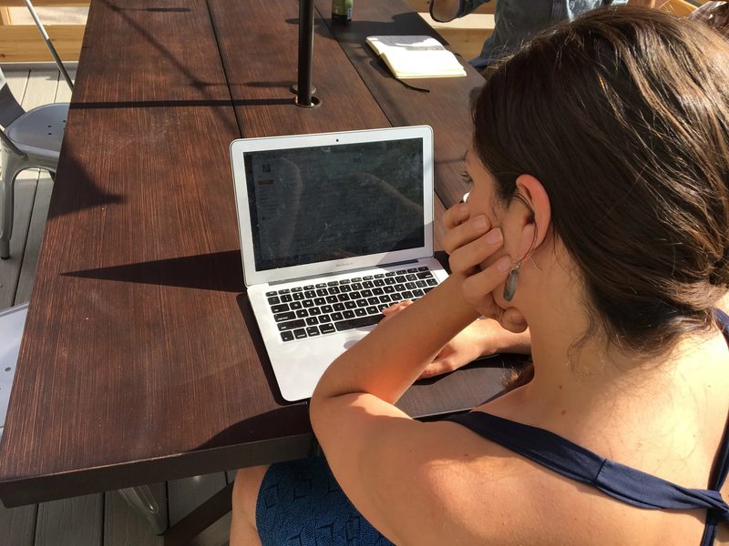 A member working on a laptop at a wooden deck table in the Colorado sun.