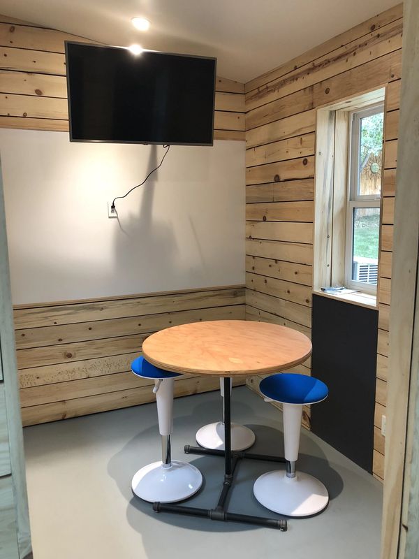 The small conference room: a round café table with seating, a wall-mounted screen, and wood-paneled walls.
